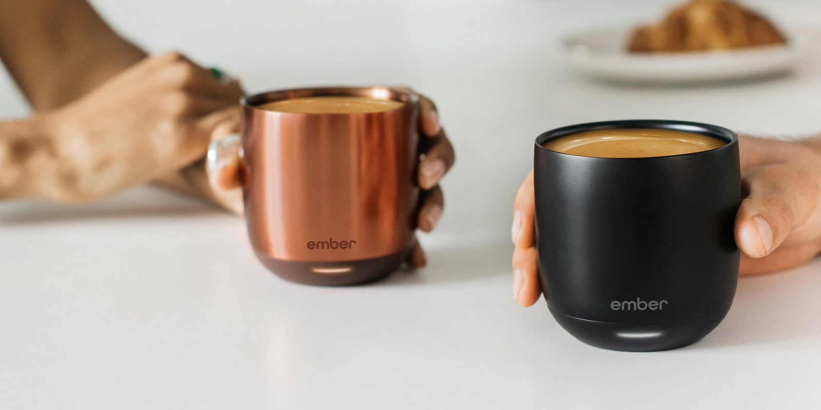 Two people hold their Ember Cup in Black and Copper Edition filled with a Cafecito.